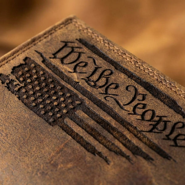 Close-up of a distressed brown leather long wallet engraved with "We The People" and an American flag.