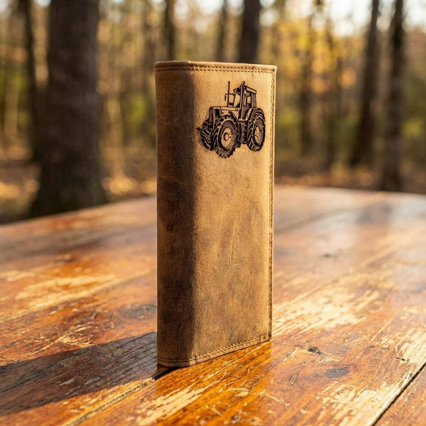 Distressed leather long wallet with a tractor engraving standing on a rustic wooden table.