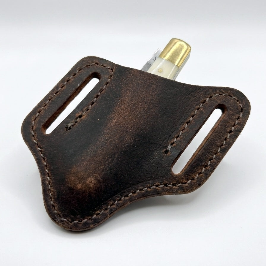 Brown leather sheath with a gold-colored clip on a white background

