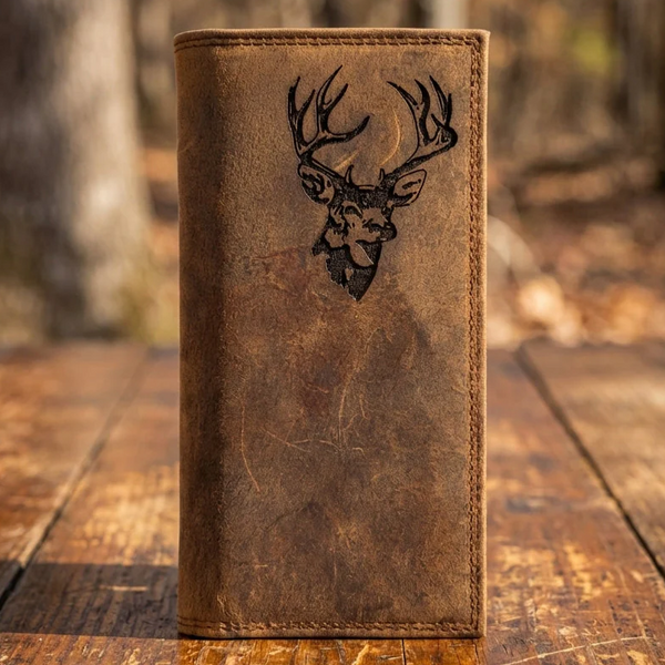 Men's distressed leather rodeo wallet with an engraved deer stag head design standing on a wooden surface.